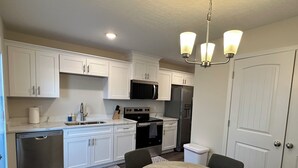 A modern kitchen with white cabinetry, stainless steel appliances, a dining area with a round table, and a chandelier. - 2-bedroom townhome in South Augusta (Augusta)