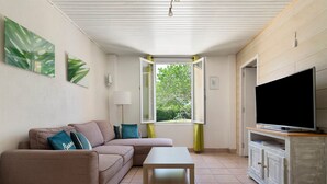 Una sala de estar con sofá, una mesa de centro, un televisor sobre un mueble bajo y una ventana con cortinas.