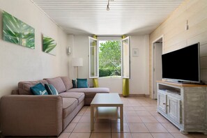 Ein Wohnzimmer mit Sofa, Couchtisch, Fernseher auf einem Schrank und einem Fenster mit Vorhängen.