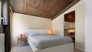 Un dormitorio con cama, mesita de noche, lámpara y techo de madera.