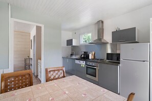 A compact kitchen with a dining table, chairs, a microwave, stove, oven, and a refrigerator. - Holiday Home La Mailleraie - L'étang with Shared Pool, Private Terrace & Wi-Fi (Valojoulx)