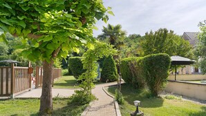 Un sendero pavimentado en un jardín ajardinado, con cercado de madera, una palmera y un edificio al fondo.