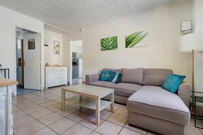 A living room with a sofa, a coffee table, and a kitchen in the background. - Holiday Home La Mailleraie - L'étang with Shared Pool, Private Terrace & Wi-Fi (Valojoulx)