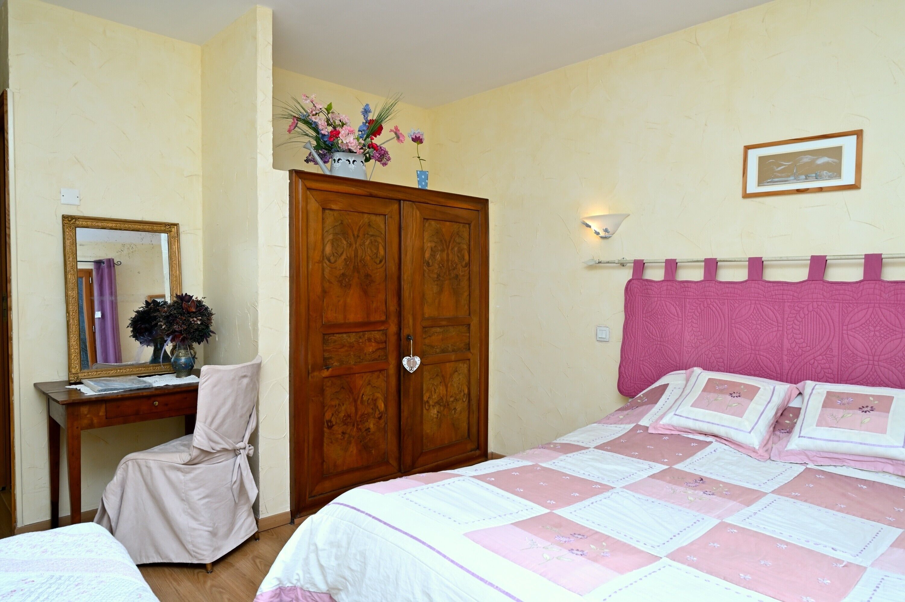 Une chambre à coucher comprenant un lit, une chaise, une armoire, un miroir et un tableau accroché au mur.