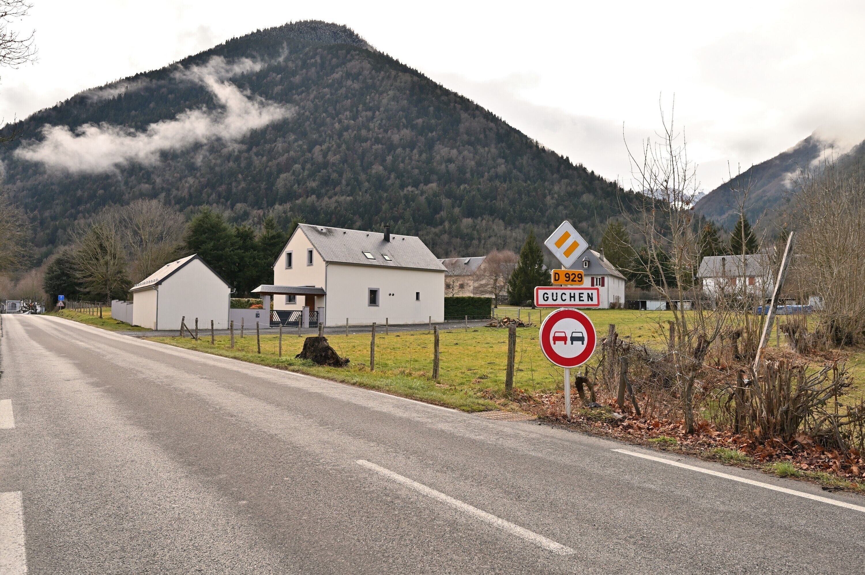 Une route de campagne avec un panneau indiquant l’interdiction d’accès, des maisons et une montagne en arrière-plan.
