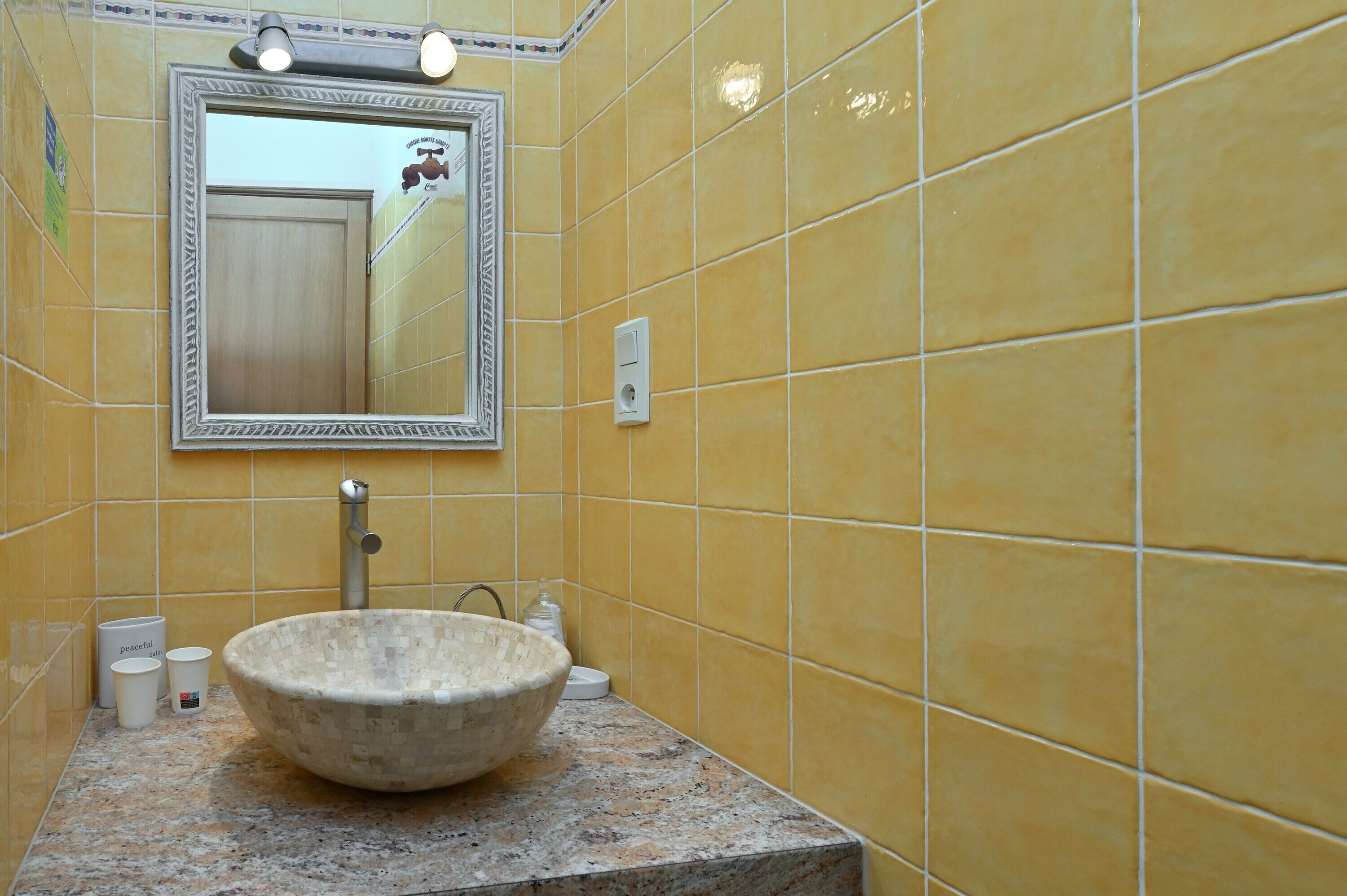 Un bagno con piastrelle gialle, un lavabo capiente, uno specchio e un rubinetto.