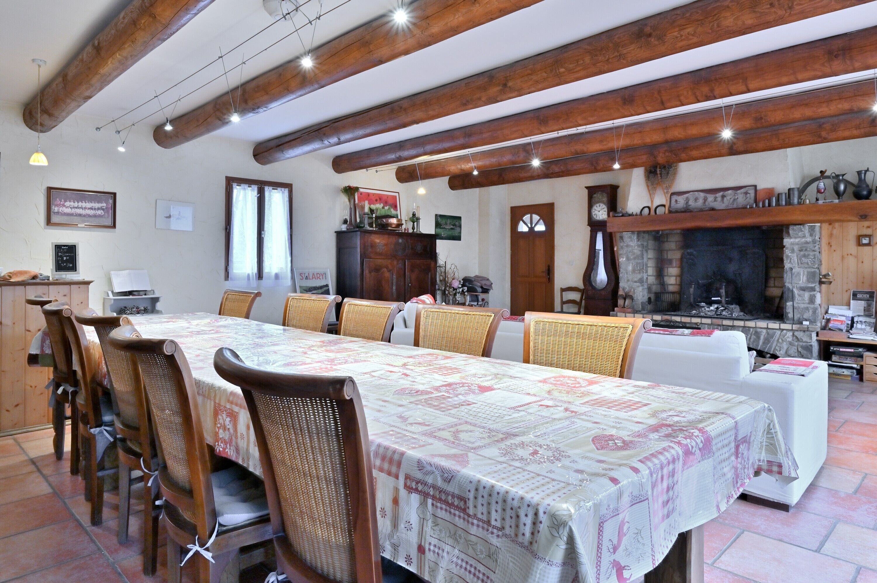 Een eethoek met een lange tafel, stoelen, een open haard en een klok aan de muur.
