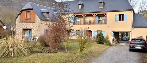 A two-story house with a stone facade, wooden balcony, and a gravel driveway.