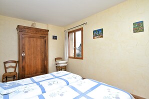 Ein Schlafzimmer mit zwei Betten, einem Holzschrank, einem Stuhl, einem Fenster mit Vorhang und zwei Wandbildern.
