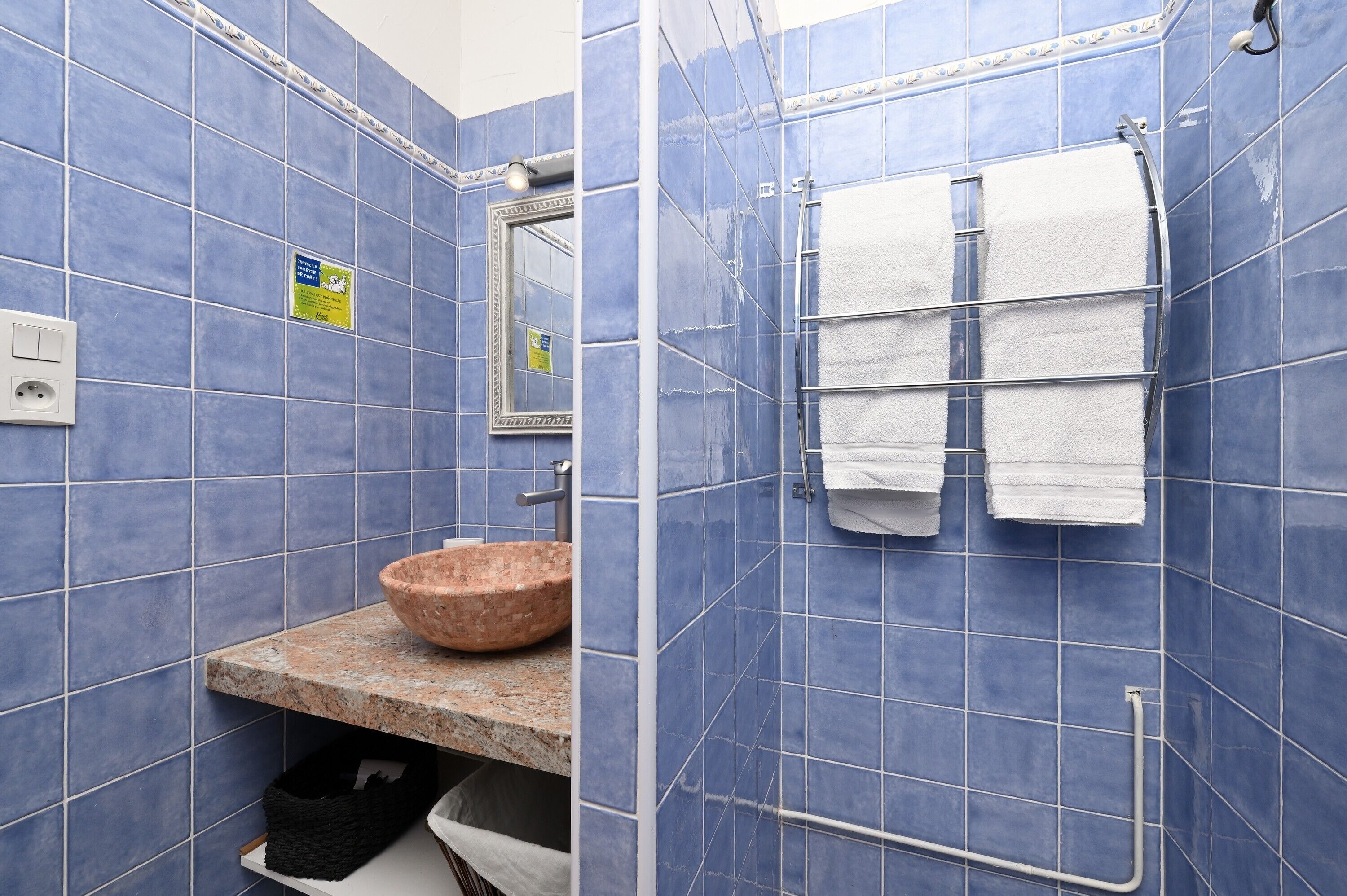 A bathroom with blue tiles, a granite countertop, a brown sink, a towel rack with white towels, and a mirror.