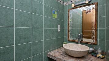 A bathroom with green tiled walls, a large mirror, a granite countertop, and a vessel sink.