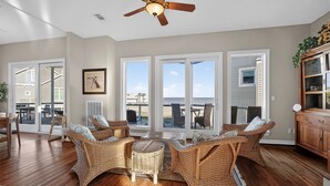 A spacious living room with wicker furniture, large windows, and a ceiling fan. - Beach Diamond - Gulf views, steps to the beach! (Galveston)