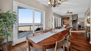 A spacious dining area with a wooden table and chairs, a chandelier, and a view of the beach through large sliding doors. - Beach Diamond - Gulf views, steps to the beach! (Galveston)