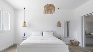 Un dormitorio con una cama blanca, dos lámparas colgantes de mimbre, una mesita de noche con un florero y una cesta tejida.