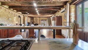 Et rustikt køkken med en stenvæg, træbjælker, en gasblus og et stort vindue.