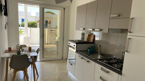 Een moderne keuken met witte kastjes, een gasfornuis en een eethoek met een tafel en stoelen.