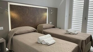Een hotelkamer met twee bedden, elk met hoofdeinde en een gewatteerde spreidek. Er liggen handdoeken op de bedden, en een nachtkastje met een lamp.