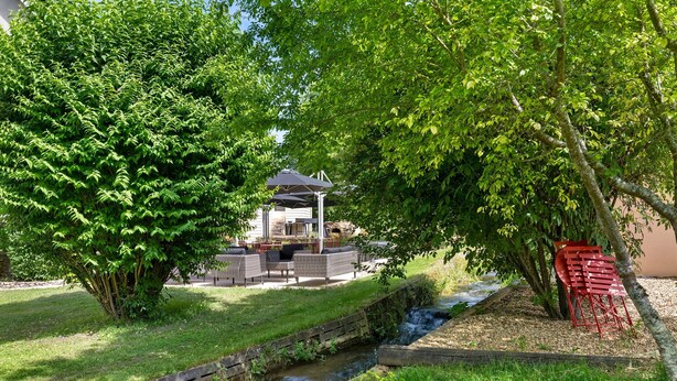 A riverside patio with outdoor seating, a small bridge, and a gazebo.