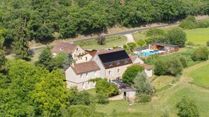 A large house with a swimming pool, surrounded by lush greenery and a winding road.