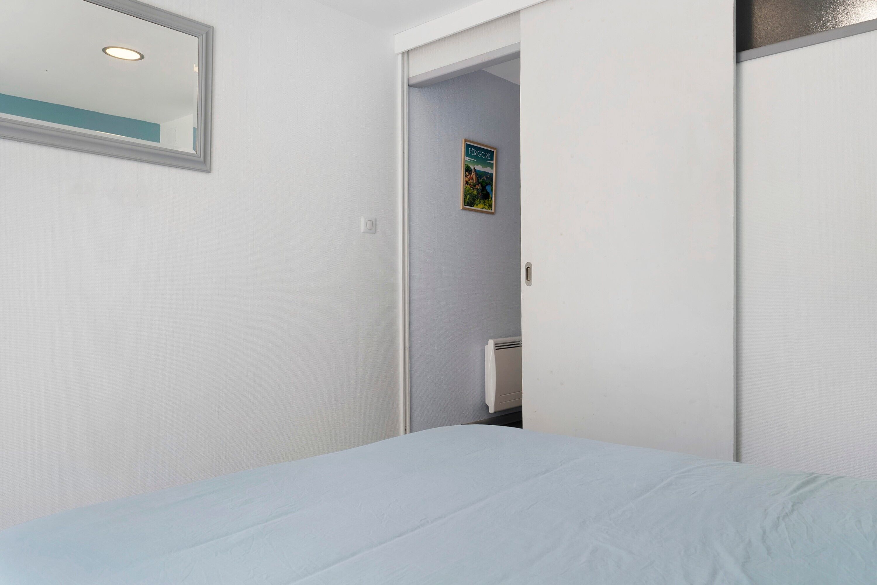 Een slaapkamer met een bed, een deur naar een badkamer en een poster aan de muur.