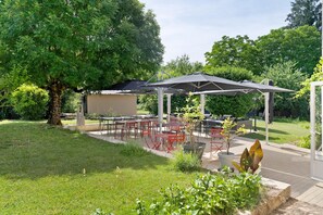 Un espace extérieur aménagé avec des tables et des chaises, un coin salon abrité et un arbre.