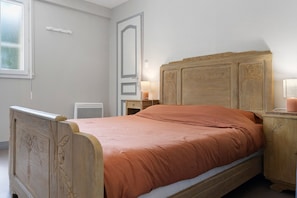 A bedroom with a wooden bed, a nightstand, a lamp, and a window. - Suite du Moulin à Vent Apartment with Shared Pool, Communal Garden and Wi-Fi (Valojoulx)