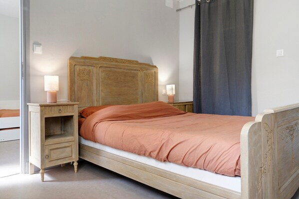 Un lit simple avec une tête de lit en bois, deux tables de chevet avec des lampes et un rideau foncé.