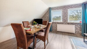 A dining area with a wooden table, four chairs, a black TV, and a window with curtains. - Apartment "Wiese" with Private Terrace, Garden and Wi-Fi (Ehndorf)