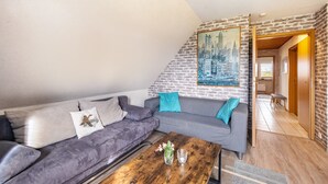 A living room with a grey sofa, a wooden coffee table, and a cityscape painting on the wall. - Apartment "Wiese" with Private Terrace, Garden and Wi-Fi (Ehndorf)