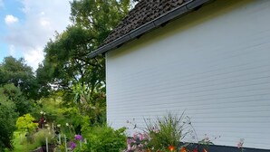 A garden with a white building, a stone pathway, and a sign with partially visible text. - Apartment "Wiese" with Private Terrace, Garden and Wi-Fi (Ehndorf)
