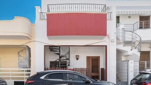 A two-story building with a white facade, a red awning, and a spiral staircase leading to a balcony.