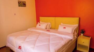 A bed with a quilted white duvet, a yellow headboard, and a small bedside table with a red logo.