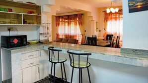 Een moderne keuken met een magnetron, barstoelen en een eethoek met een bank en gordijnen.