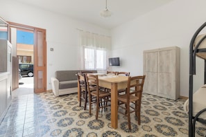 A dining area with a wooden table and chairs, a sofa, a television on the wall, and a patterned floor. - Casa Poesia - Trilo PT by BarbarHouse (Torre Lapillo)