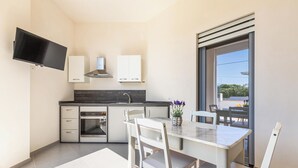 Eine moderne Küche mit Flachbildfernseher, weißen Schränken, Backofen und einem Essbereich mit Tisch und Stühlen.