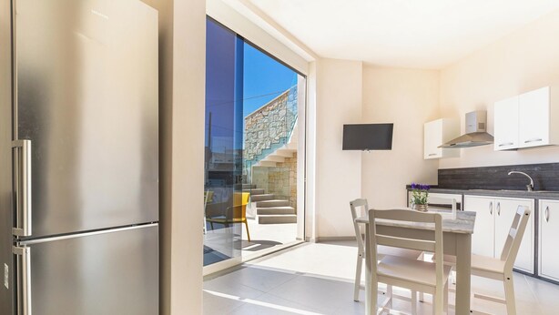 Eine moderne Küche mit einem Edelstahlkühlschrank, einem Esstisch mit Stühlen, einem flachbildfernseher über der Arbeitsfläche und einer Treppe, die in einen Außenbereich führt.