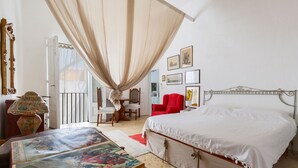 Una camera da letto con un letto grande, una sedia rossa, un tavolo con una stampa colorata e un balcone con una porta bianca.