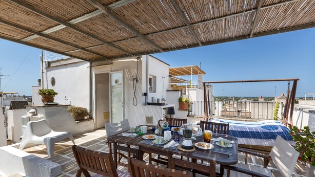Una terrazza sul tetto con un tavolo da pranzo per quattro persone, circondato da sedie bianche.