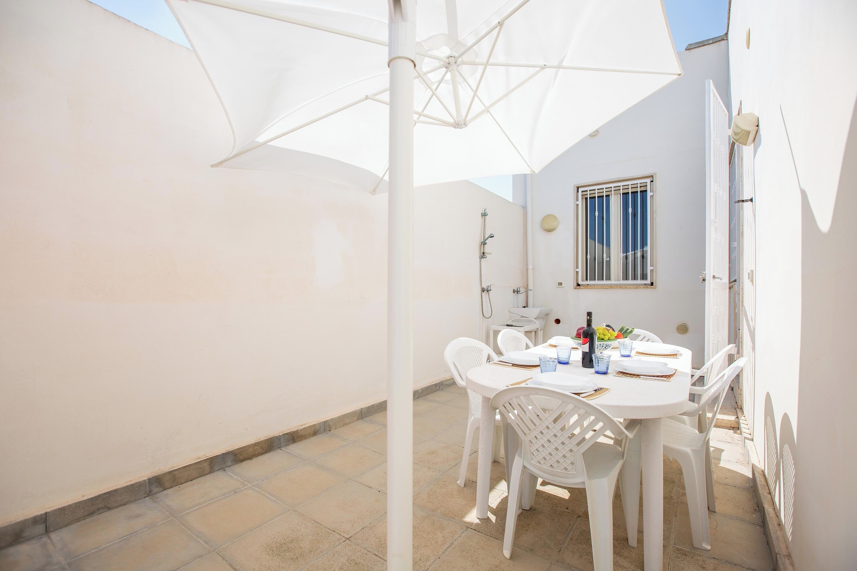 Une terrasse extérieure blanche avec une table ronde, des chaises blanches et un grand parasol.