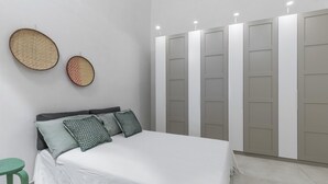 A bedroom with a bed, pillows, a green stool, and a wardrobe with multiple doors. - Casa della Farfalla by BarbarHouse (Polignano a Mare)