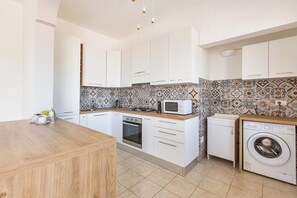 A modern kitchen with white cabinets, a wooden countertop, a microwave, a stove, and a washing machine. - Salento Essentiae by BarbarHouse (Torre Suda)