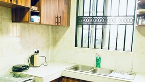 Una cocina con salpicadero de mármol, armarios de madera, una ventana con celosías decorativas, un lavamanos y una encimera con un hervidor y un teléfono.