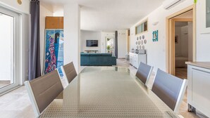 Ein moderner Essbereich mit einem Glastisch, Metallstühlen, einer Couch und einer Küche im Hintergrund.