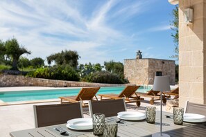 A poolside dining area with tables set for two, lounge chairs, and a stone building in the background. - Villa Matilda by Perle di Puglia (Ostuni)
