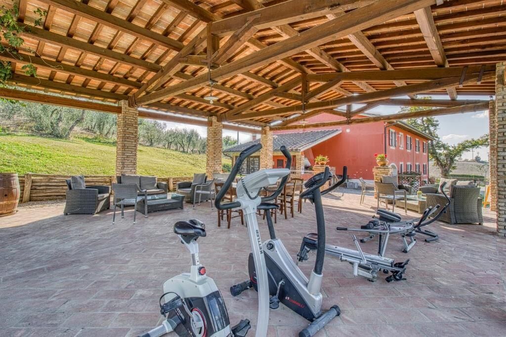 Un área de gimnasio al aire libre con equipo de ejercicio, asientos y un porche cubierto.