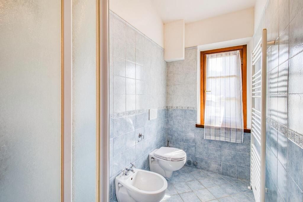 A bathroom with two toilets, a bidet, and a window with a wooden frame.