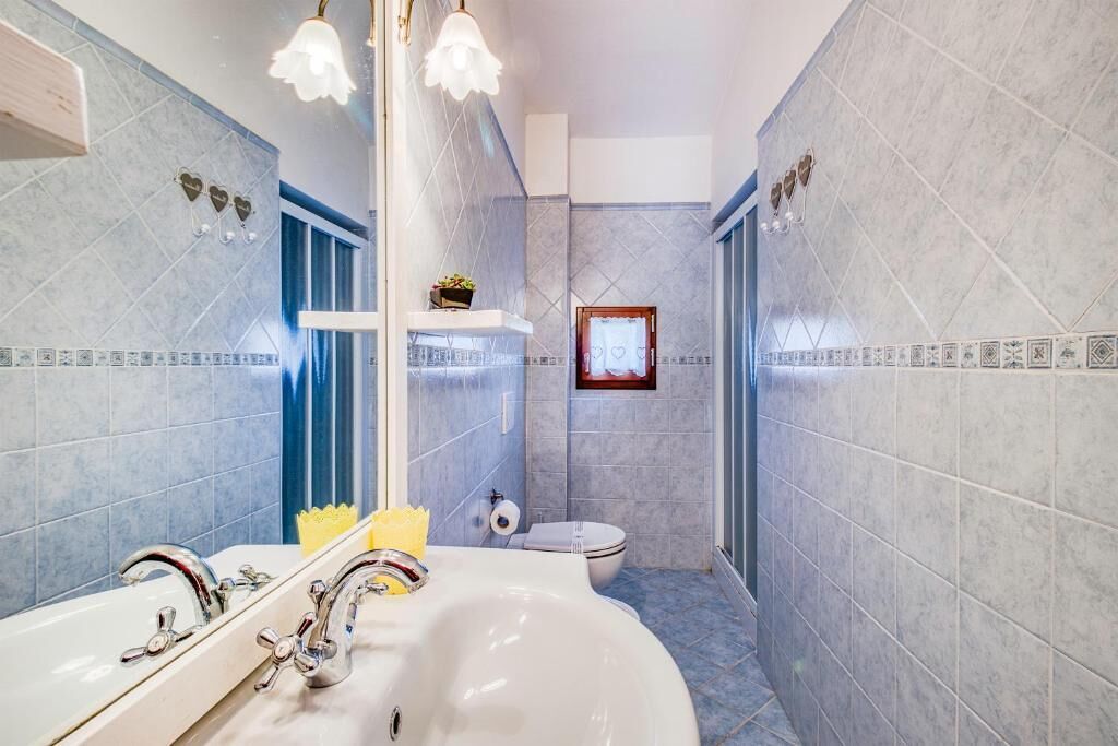 Un baño con un lavamanos blanco, dos grifos, un espejo y un inodoro.