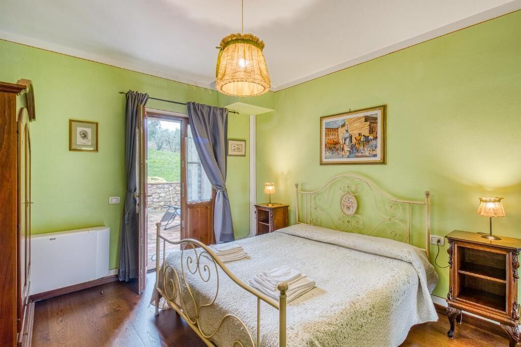 Une chambre à coucher comprenant un lit, une table de chevet, une lampe, une fenêtre avec des rideaux et une porte donnant sur un espace extérieur.