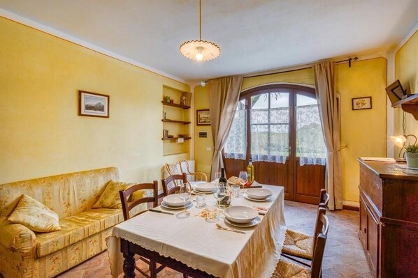 A dining area with a table set for four, a sofa, and a window with curtains. - Agriturismo Rebarco (Castelfiorentino)