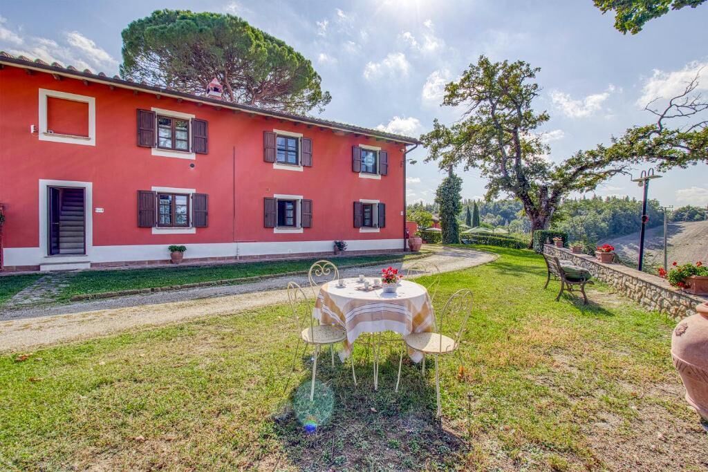 A red villa with a garden, a table with chairs, and a view of the countryside.
